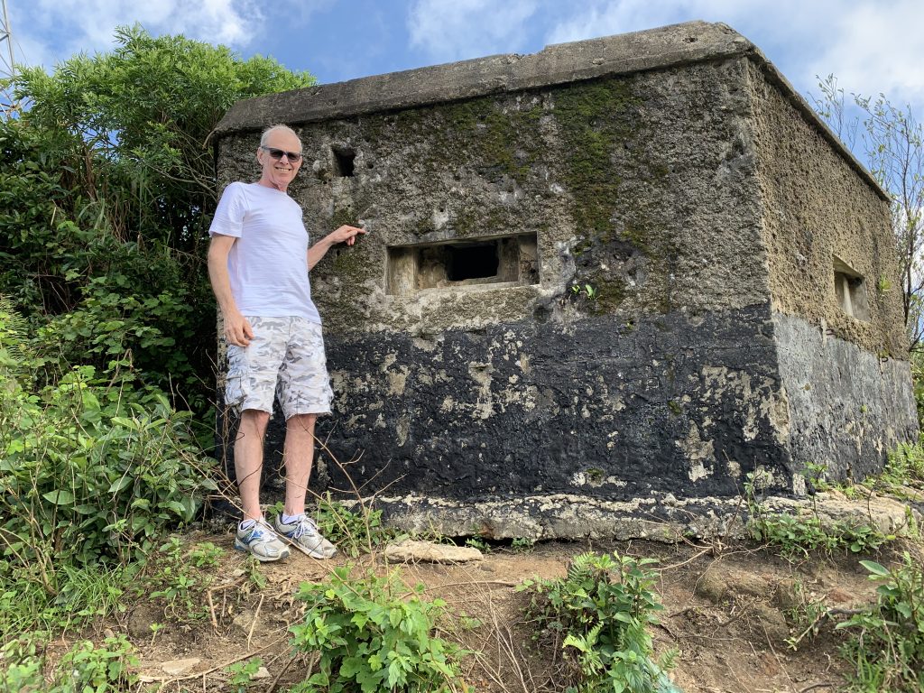 Hai Van Pass, Vietnam. Gary is standing in front of a war bunker full of bullet holes. He is pointing to a lodged bullet slug.